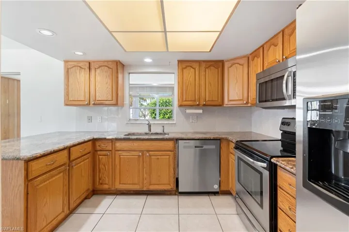 Kitchen with open floor plan, appliances with stainless steel finishes, brown cabinetry, a raised ceiling, and a sink