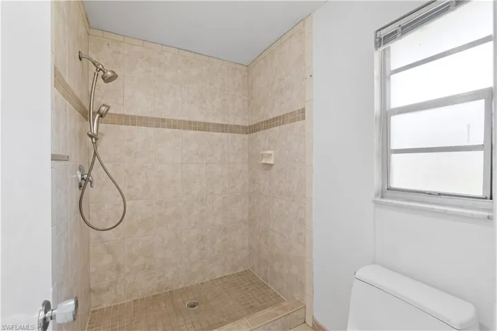 Full primary bath featuring toilet, a healthy amount of sunlight, and a tile shower