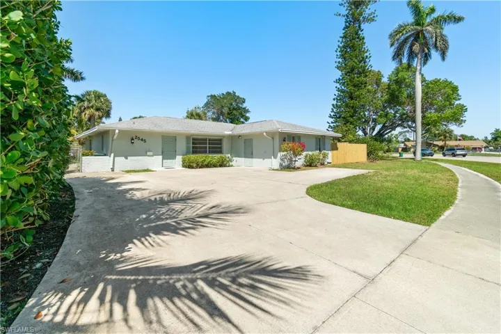 Ranch-style house with stucco siding, curved driveway, a front lawn, and fence