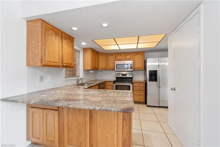 Kitchen with light stone counters, a peninsula, light tile patterned flooring, a sink, and appliances with stainless steel finishes