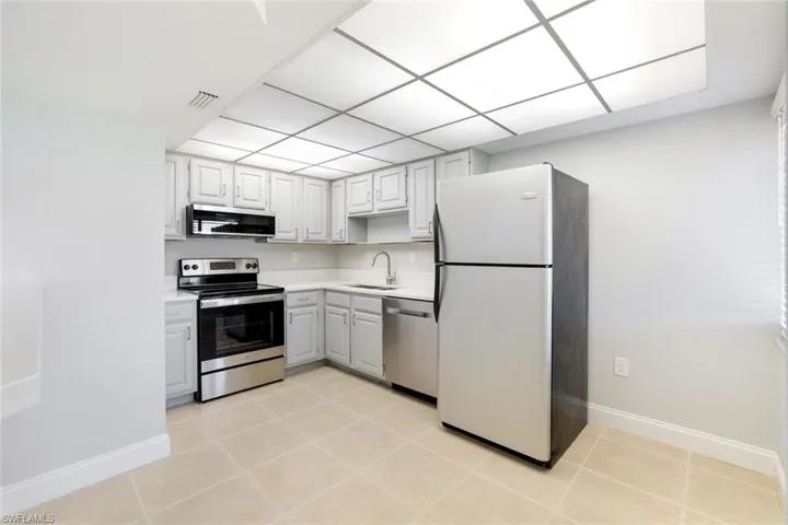 Kitchen with appliances with stainless steel finishes, light countertops, light tile patterned floors, range hood, and white cabinetry