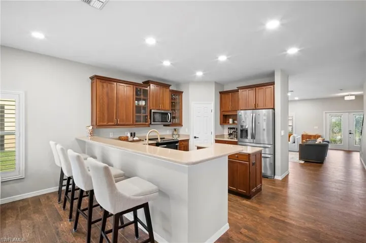Kitchen featuring glass insert cabinets, brown cabinetry, a kitchen breakfast bar, appliances with stainless steel finishes, and a peninsula