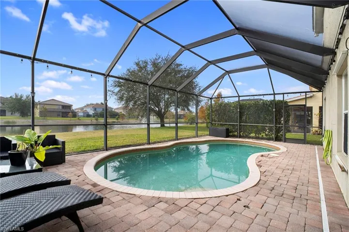 Outdoor pool featuring a sunroom, glass enclosure, a water view, a patio, and a yard