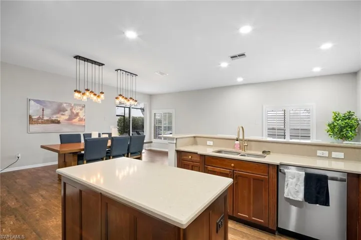 Kitchen featuring dishwasher, a kitchen island, decorative light fixtures, dark wood finished floors, and light stone counters