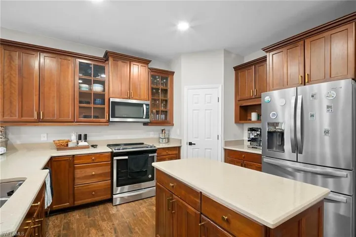 Kitchen featuring stainless steel appliances, a kitchen island, glass insert cabinets, dark wood-type flooring, and brown cabinetry