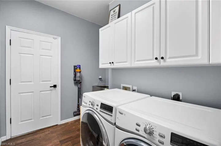 Laundry room with dark wood-type flooring, cabinet space, and washing machine and dryer