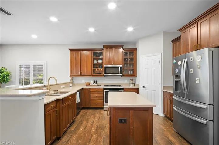 Kitchen with glass insert cabinets, stainless steel appliances, recessed lighting, brown cabinets, and dark wood-style flooring
