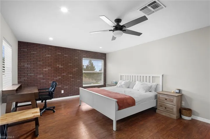 Bedroom featuring brick wall, a desk, dark wood finished floors, a ceiling fan, and an accent wall