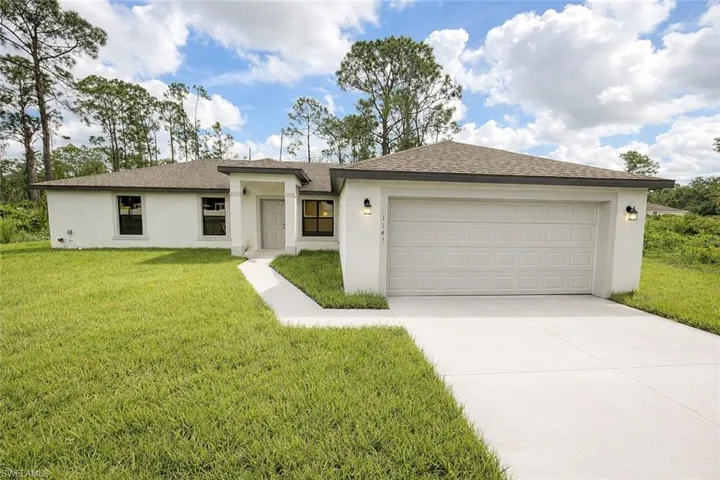 View of front of property with a front yard, concrete driveway, a garage, stucco siding, and roof with shingles