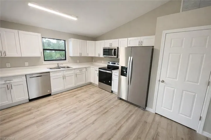 Kitchen featuring stainless steel appliances, vaulted ceiling, white cabinetry, light countertops, and light wood-style flooring