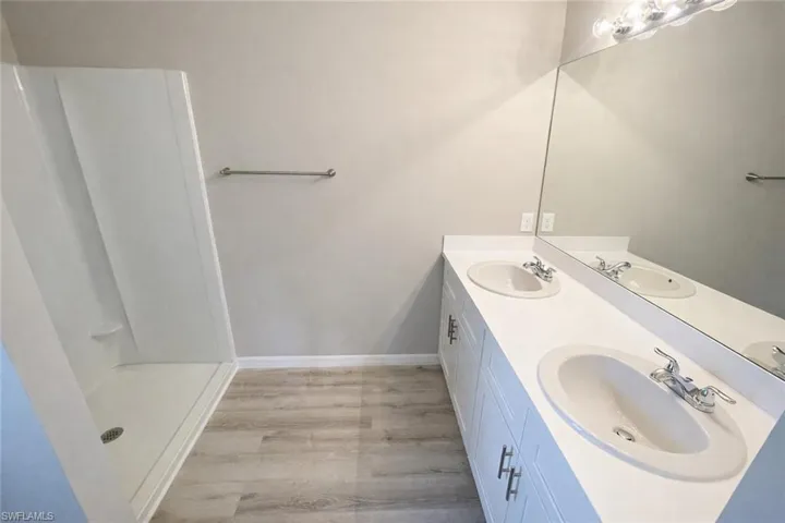 Bathroom with double vanity, light wood-style flooring, and a shower stall