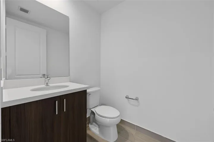 Half bath with vanity, toilet, baseboards, wood tiled floor, and visible vents