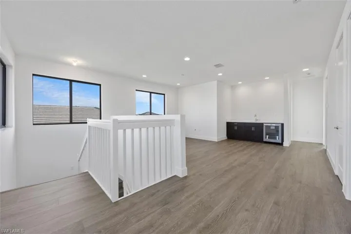 Empty room with light wood-style floors, indoor wet bar, recessed lighting, wine cooler, and visible vents