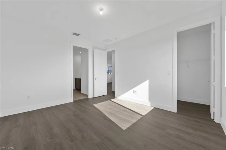 Unfurnished bedroom featuring a walk in closet, visible vents, baseboards, a closet, and dark wood-style floors