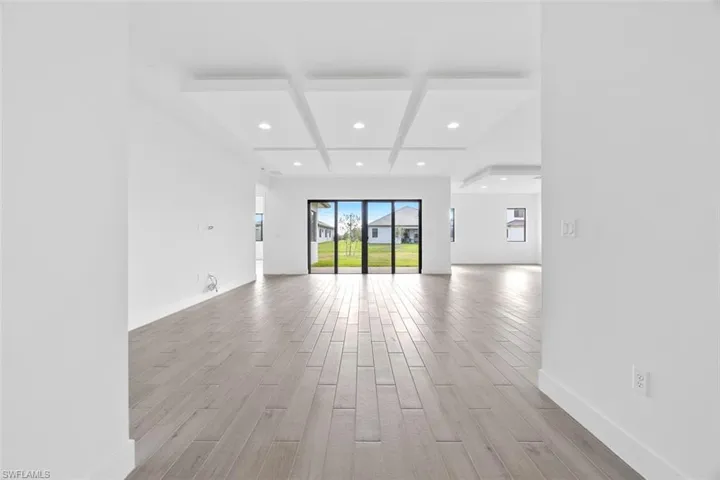 Unfurnished living room featuring baseboards, beamed ceiling, coffered ceiling, recessed lighting, and light wood-style flooring