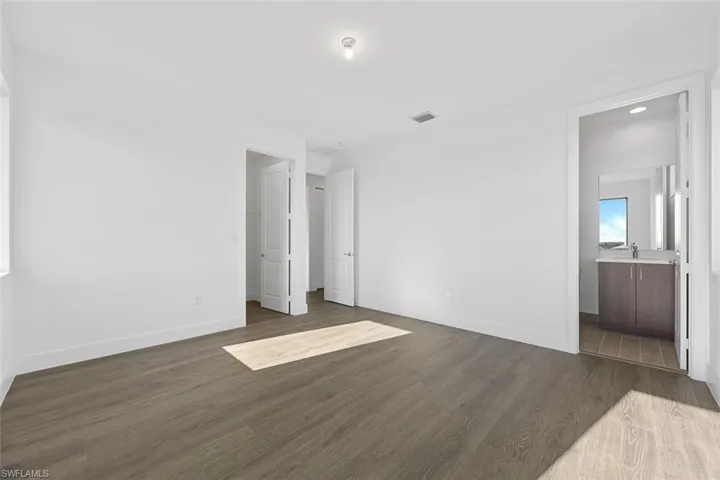 Unfurnished bedroom with a sink, ensuite bath, baseboards, visible vents, and dark wood-style floors