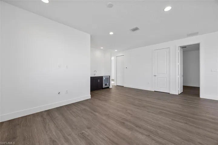 Unfurnished living room with beverage cooler, dark wood finished floors, indoor wet bar, baseboards, and visible vents
