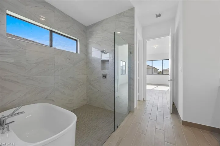 Full bath featuring a soaking tub, wood finish floors, walk in shower, and a wealth of natural light