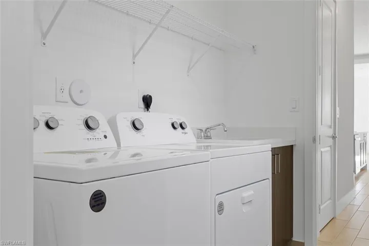 Clothes washing area featuring laundry area, a sink, light tile patterned floors, and washing machine and clothes dryer