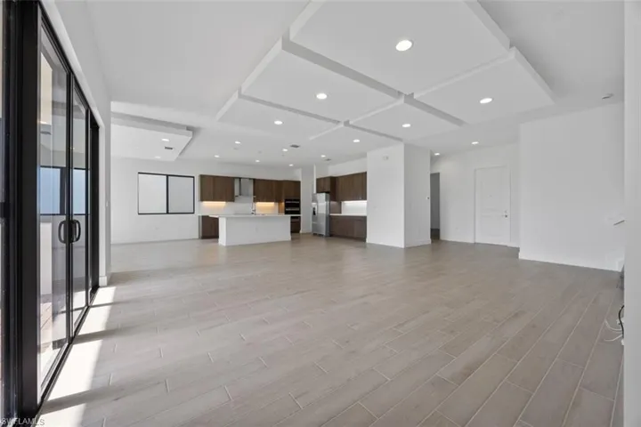 Unfurnished living room with light wood-type flooring, recessed lighting, coffered ceiling, and baseboards