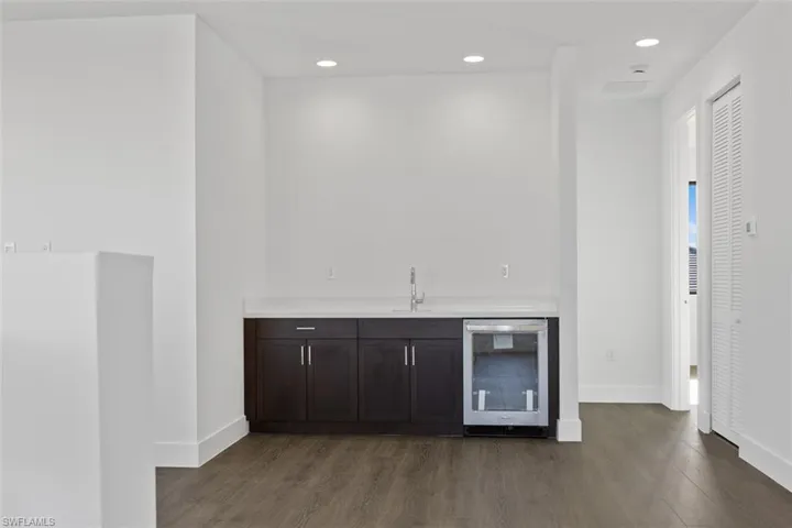 Bar with indoor wet bar, baseboards, wine cooler, and dark wood-style floors