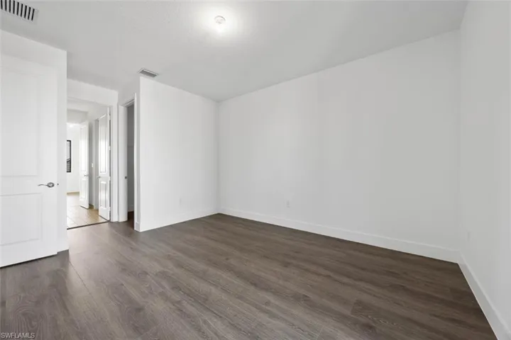 Unfurnished room with baseboards, visible vents, and dark wood-type flooring