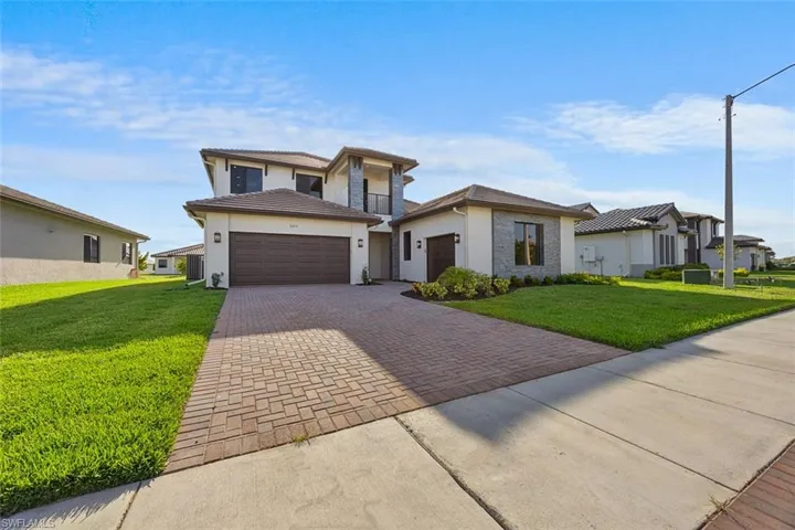 Prairie-style house featuring a front lawn, decorative driveway, stucco siding, an attached garage, and a tile roof
