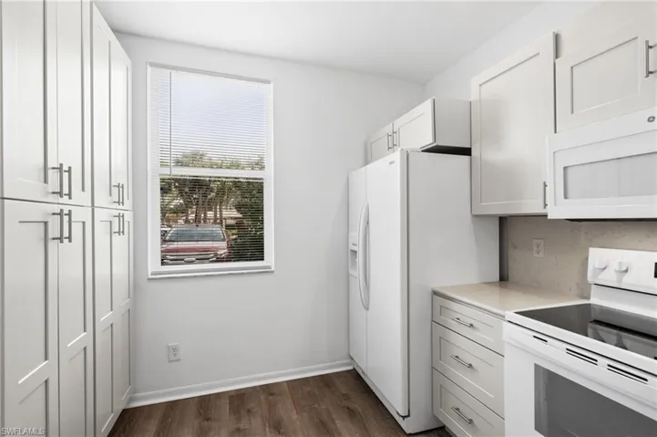 Kitchen with white appliances, dark hardwood / wood-style floors, white cabinetry, and backsplash