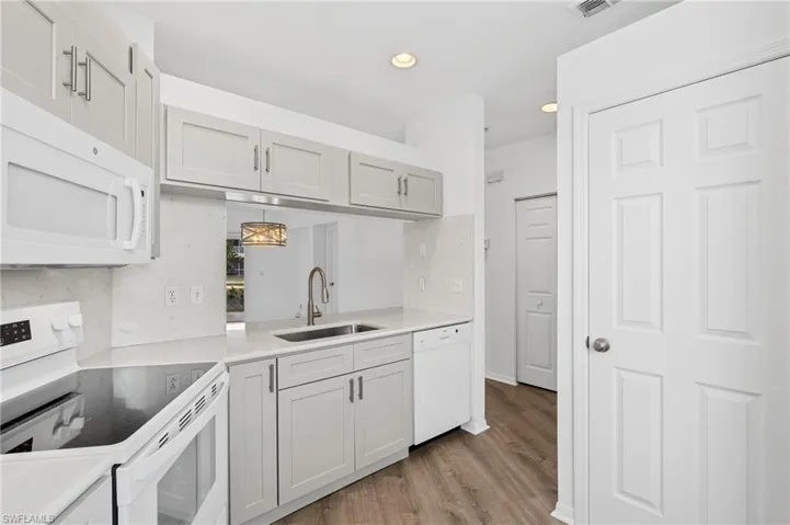 Kitchen with decorative light fixtures, light wood-type flooring, white appliances, and sink