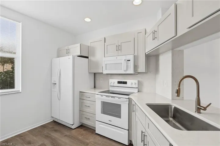 Kitchen featuring white cabinetry, sink, wood-type flooring, and white appliances
