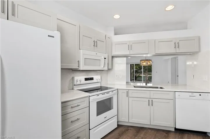 Kitchen featuring sink, hanging light fixtures, dark hardwood / wood-style flooring, white appliances, and white cabinets