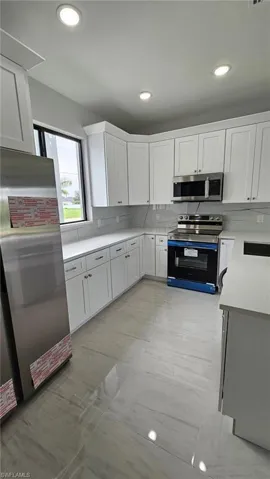 Kitchen featuring white cabinetry, appliances with stainless steel finishes, backsplash, sink, and light tile flooring