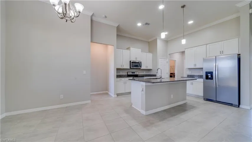The expansive open-concept room features light-colored tile flooring, high ceilings with crown molding, and a chandelier in the dining area