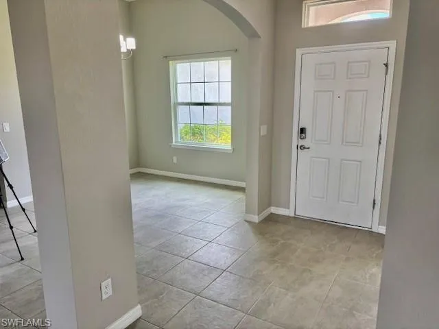 Entryway featuring light-toned tile flooring, a paneled front door with smart lock, and an arched transom window above