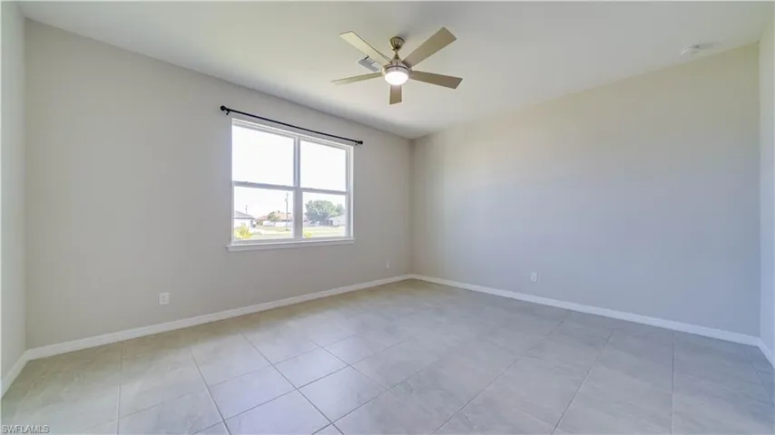 This spacious room features light-colored walls, tile flooring, and a window providing natural light