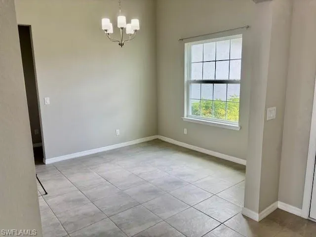 Spacious interior room featuring neutral paint, tile flooring, a multi-light chandelier, a large window with white trim, and white baseboards