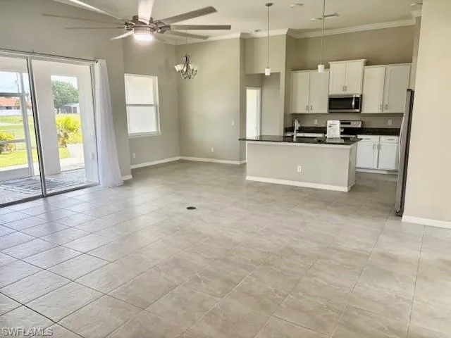 Open-concept living area featuring light-toned tile flooring, direct patio access via sliding glass doors, a modern kitchen with white cabinetry, dark countertops, and stainless steel appliances, and high ceilings with recessed lighting and a ceiling fan