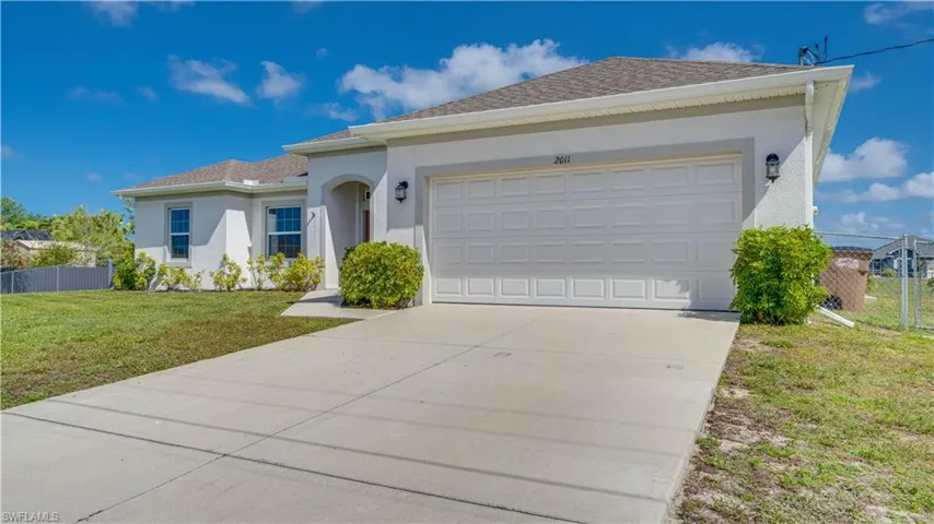 The property features a concrete driveway leading to an attached garage, a stucco exterior, and a well-maintained lawn