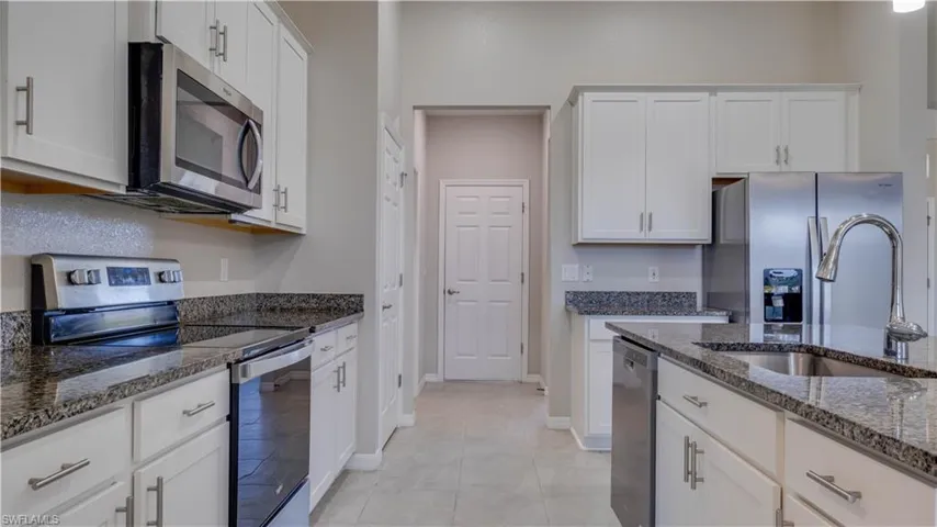 The kitchen features white cabinetry, granite countertops, and stainless steel appliances, including a microwave, range, dishwasher, and refrigerator
