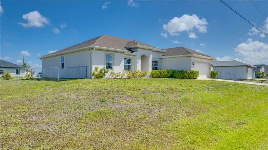 The property features a well-maintained exterior with a brown shingle roof, light-colored stucco walls, and a green lawn