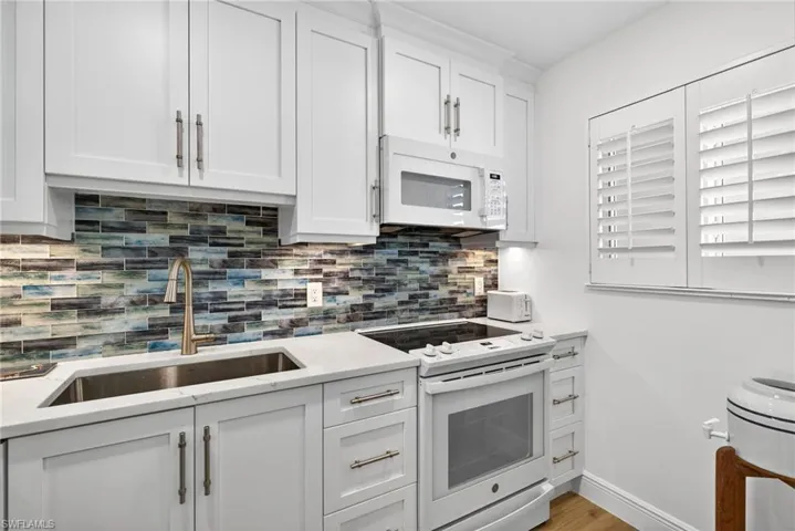 Kitchen with white appliances, white cabinets, light stone counters, light wood-type flooring, and tasteful backsplash
