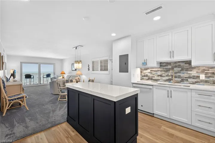 Kitchen with open floor plan, white dishwasher, light stone counters, light wood finished floors, and dual tone cabinetry