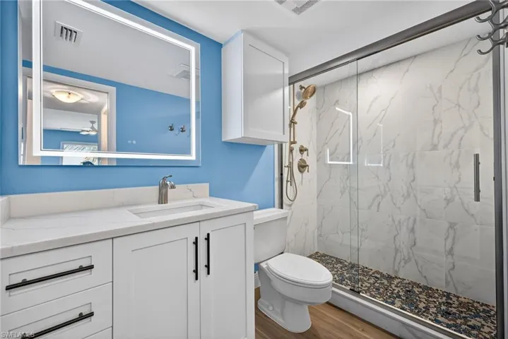Full bathroom with a marble finish shower, vanity, and wood finished floors