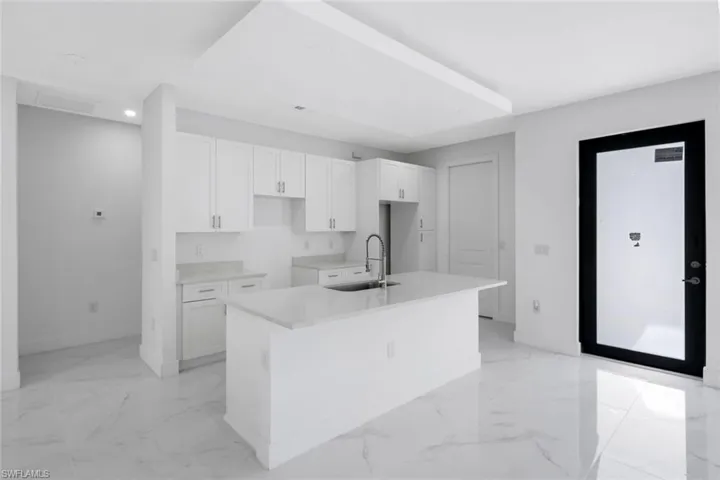 Kitchen featuring white cabinetry, an island with sink, light stone counters, recessed lighting, and light marble finish floors