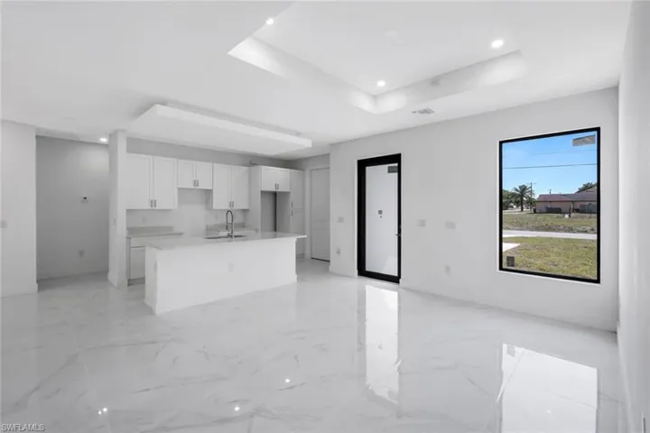 Kitchen with white cabinets, an island with sink, a raised ceiling, open floor plan, and recessed lighting