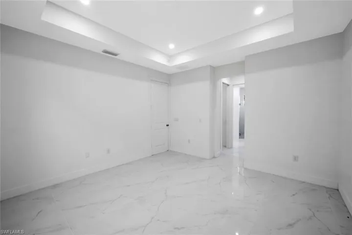 Empty room featuring a raised ceiling, recessed lighting, and light marble finish flooring