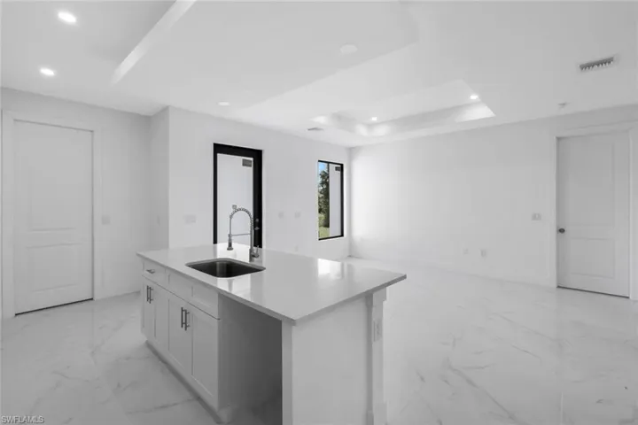 Kitchen with a kitchen island with sink, light stone countertops, a raised ceiling, recessed lighting, and white cabinetry