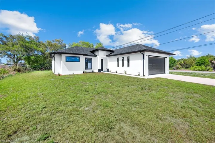 Prairie-style home with stucco siding, a front yard, an attached garage, and driveway