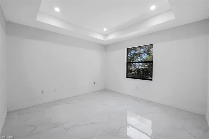 Empty room featuring recessed lighting, light marble finish flooring, and a raised ceiling