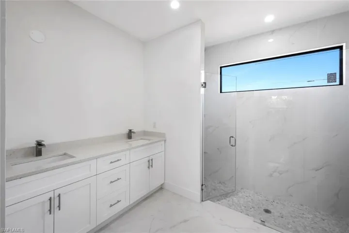 Bathroom with double vanity, a marble finish shower, light marble finish flooring, and recessed lighting